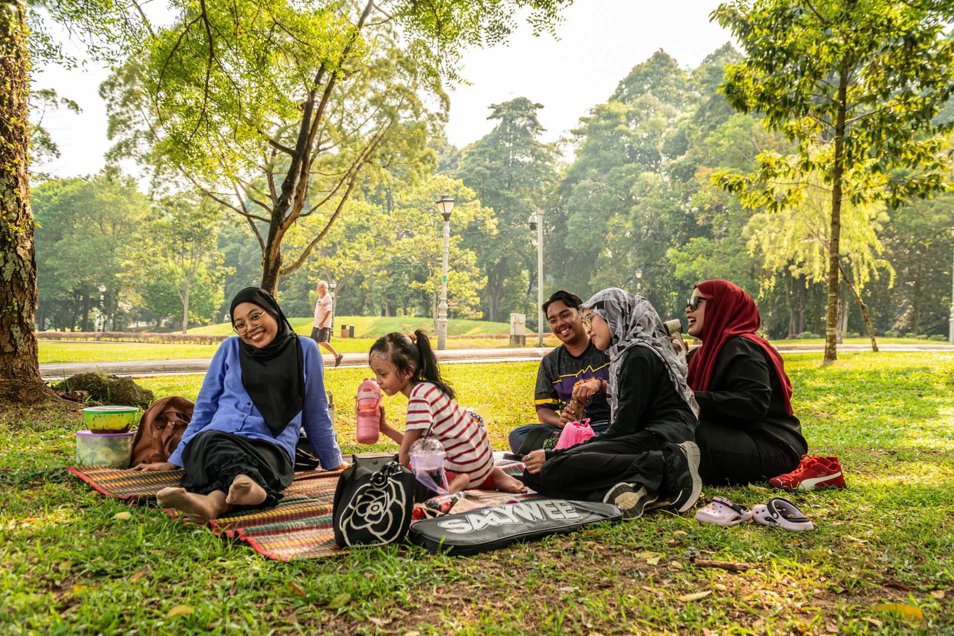 Keluarga duduk bersama di atas alas piknik di taman yang rindang